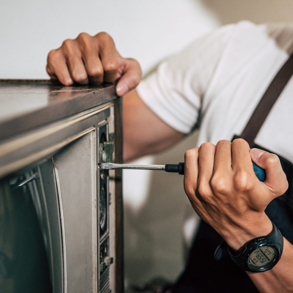 The mechanic uses a screwdriver to tighten the screws on the TV. Selective focus.