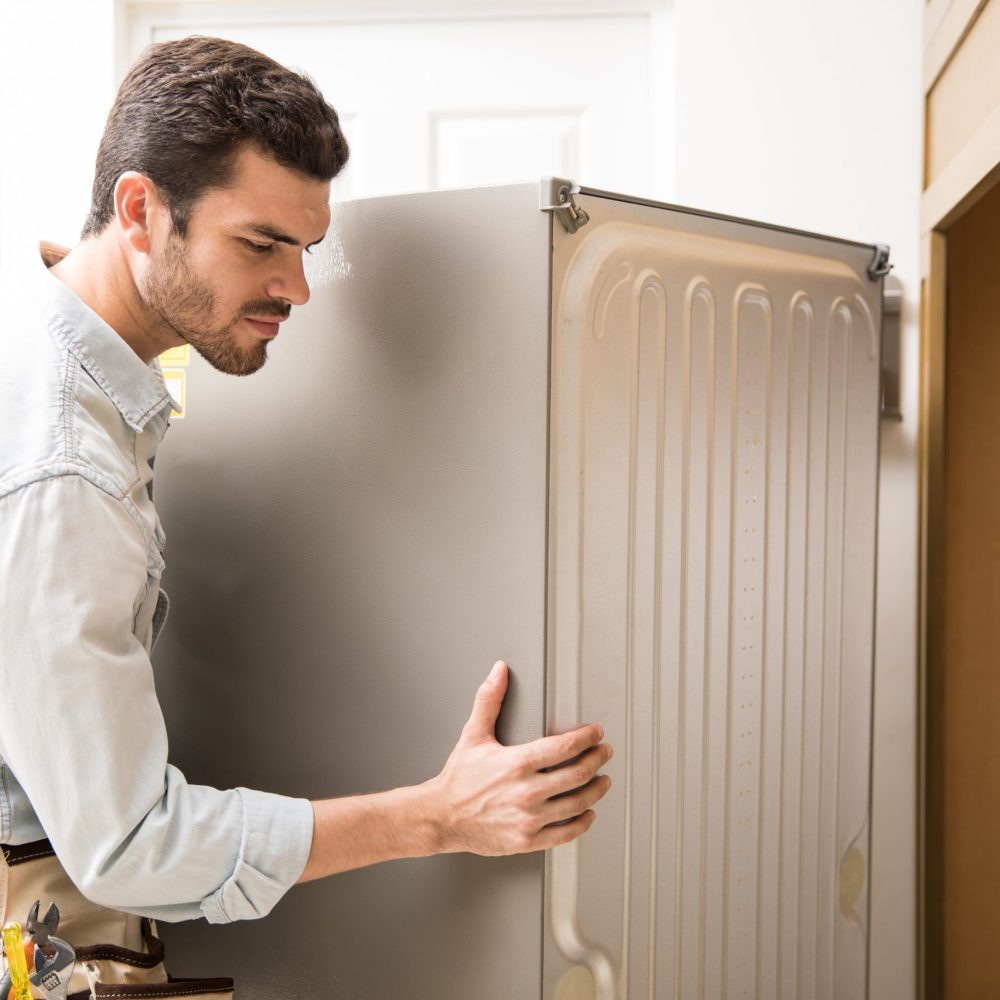 Young man working as an electrician exposing the back of a fridge to check and repair it
